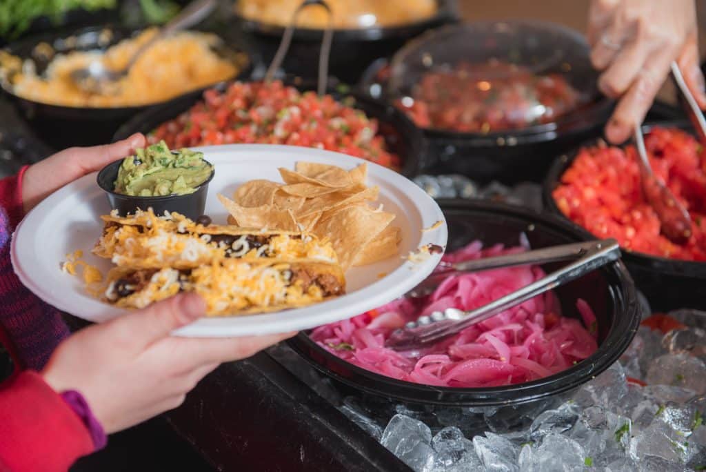 A person holds a plate filled with various dishes at a buffet, showcasing a colorful array of food options.