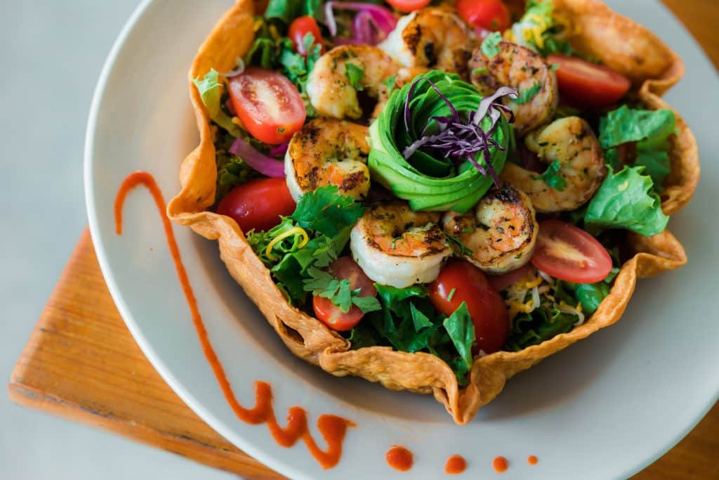 An entrée with shrimp, tomatoes, and leafy greens in a burrito bowl.